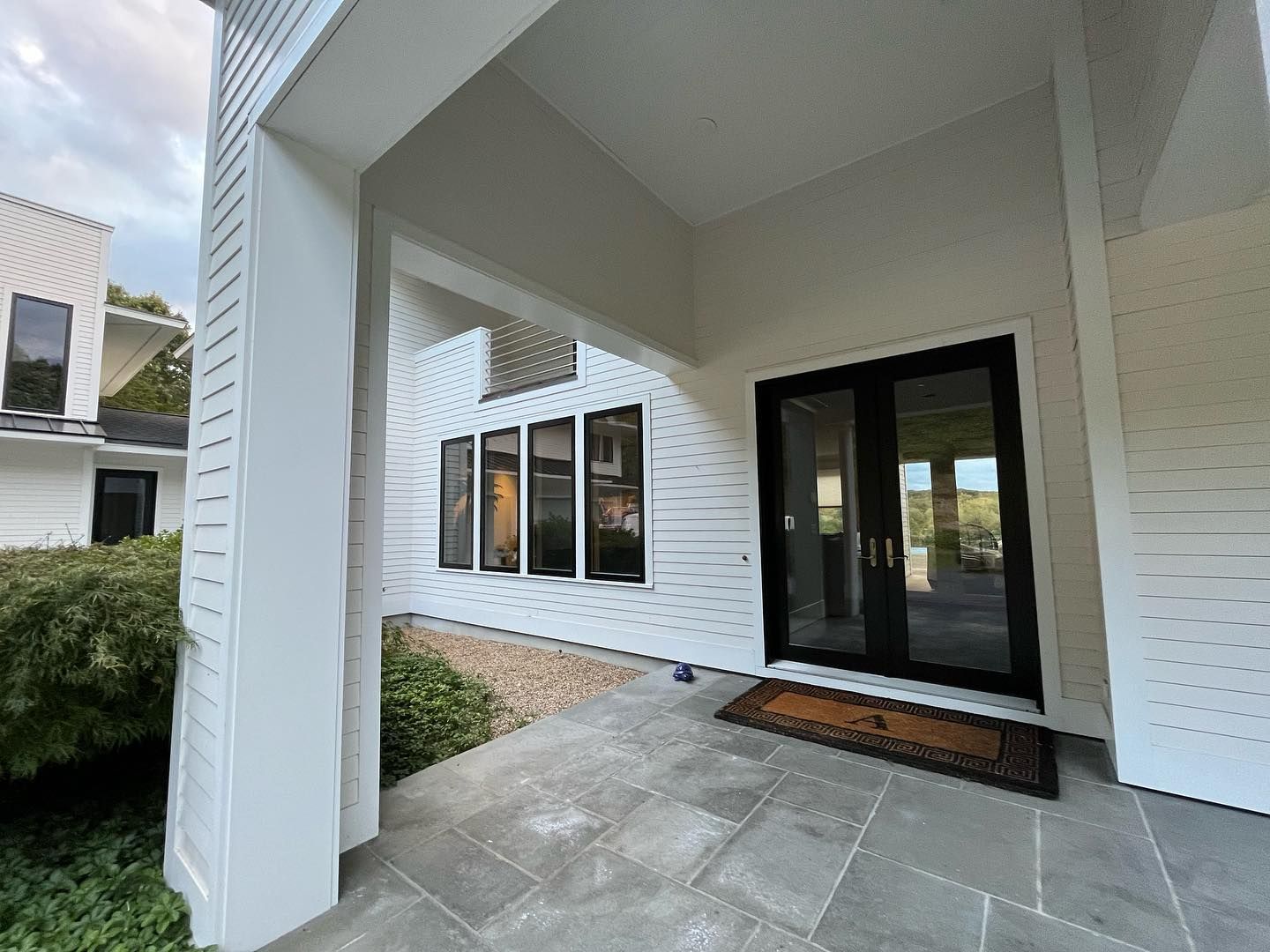 Covered entrance to a white house with black-framed glass doors and windows, and a gray stone porch.