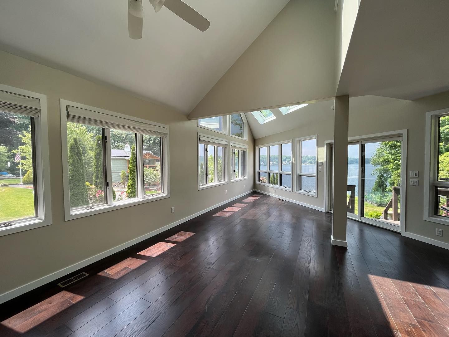 Sunroom with dark wood floors, large windows, and a view of trees and water.