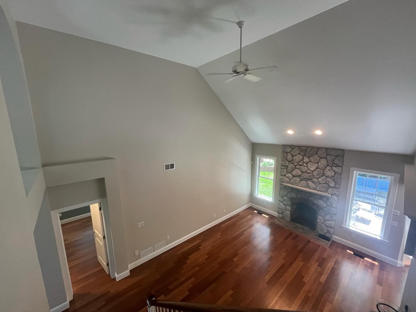 Interior view of a living room with vaulted ceiling, hardwood floors, stone fireplace, and windows.