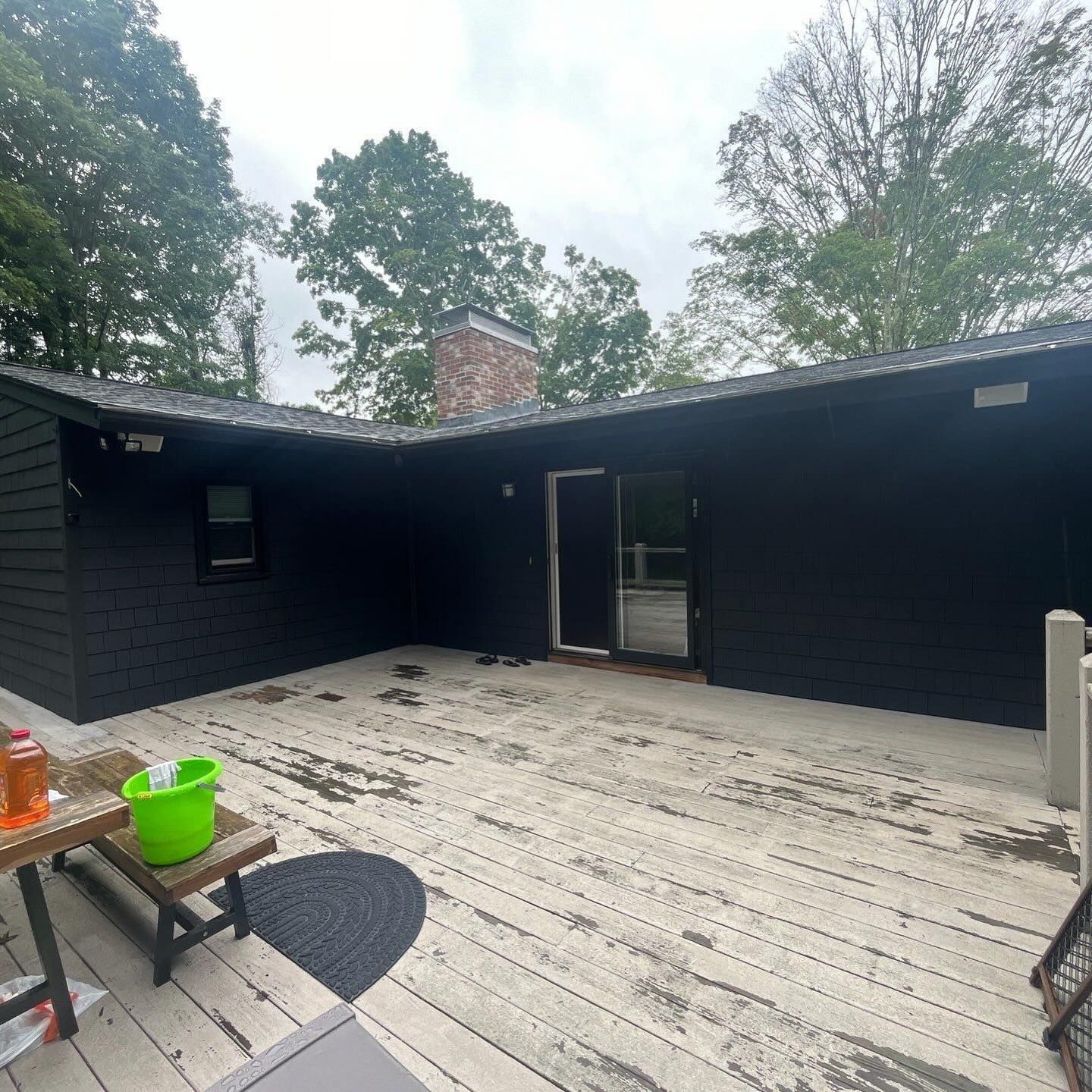 Black house exterior with a weathered wooden deck and surrounding trees.