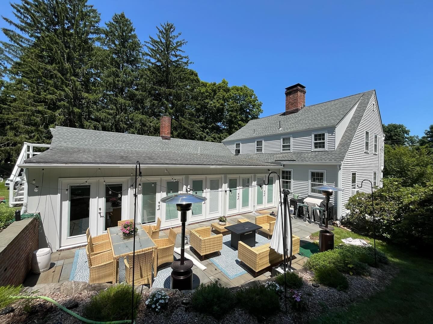 Patio of a house with outdoor furniture, heaters, and multiple doors under a blue sky.