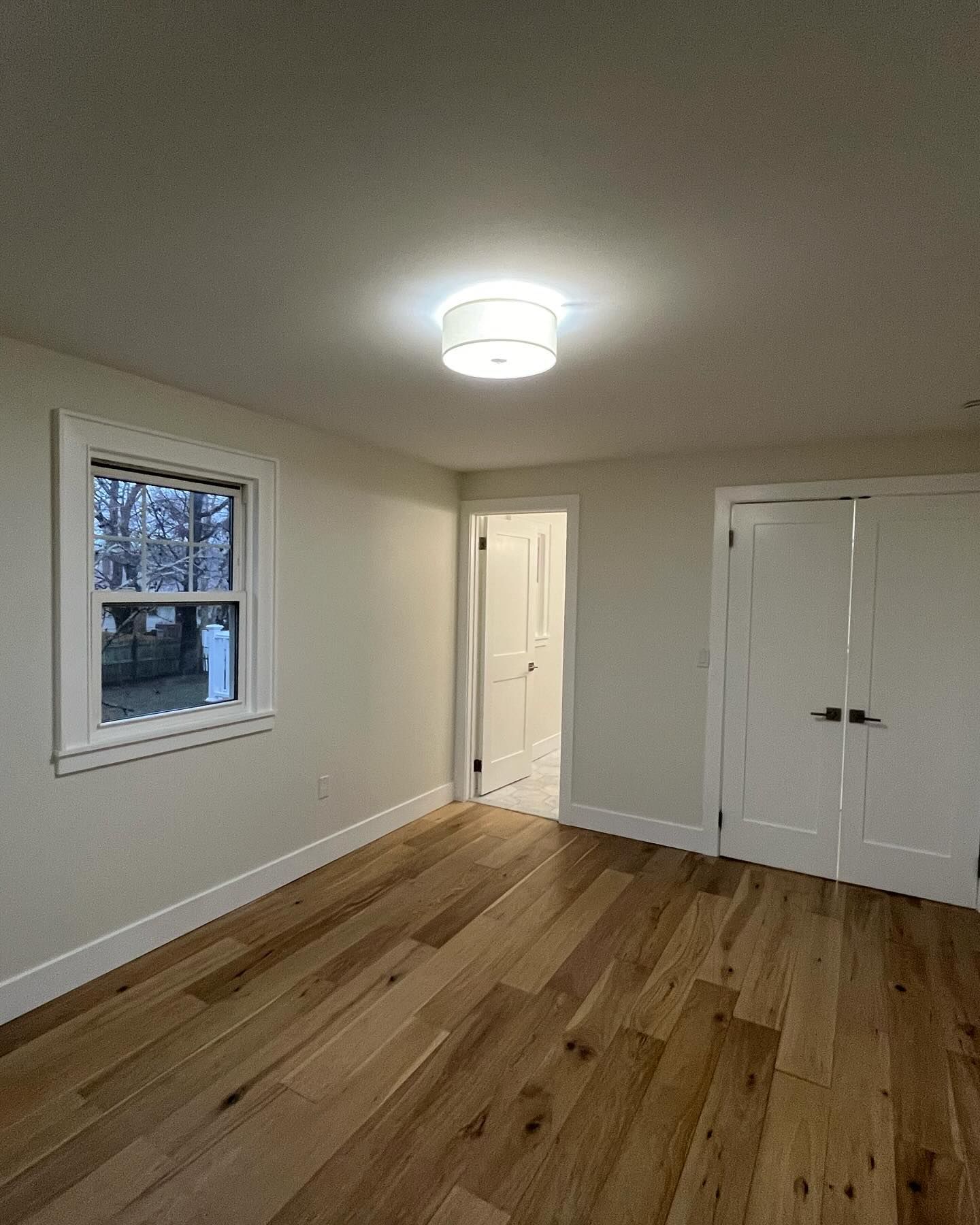 Empty room with hardwood floors, a window, doors, and a ceiling light.