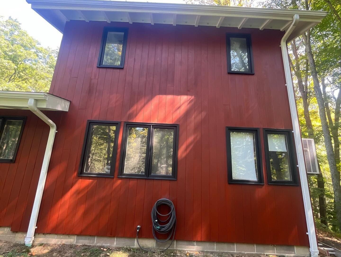 Red two-story house with black-framed windows, surrounded by trees.