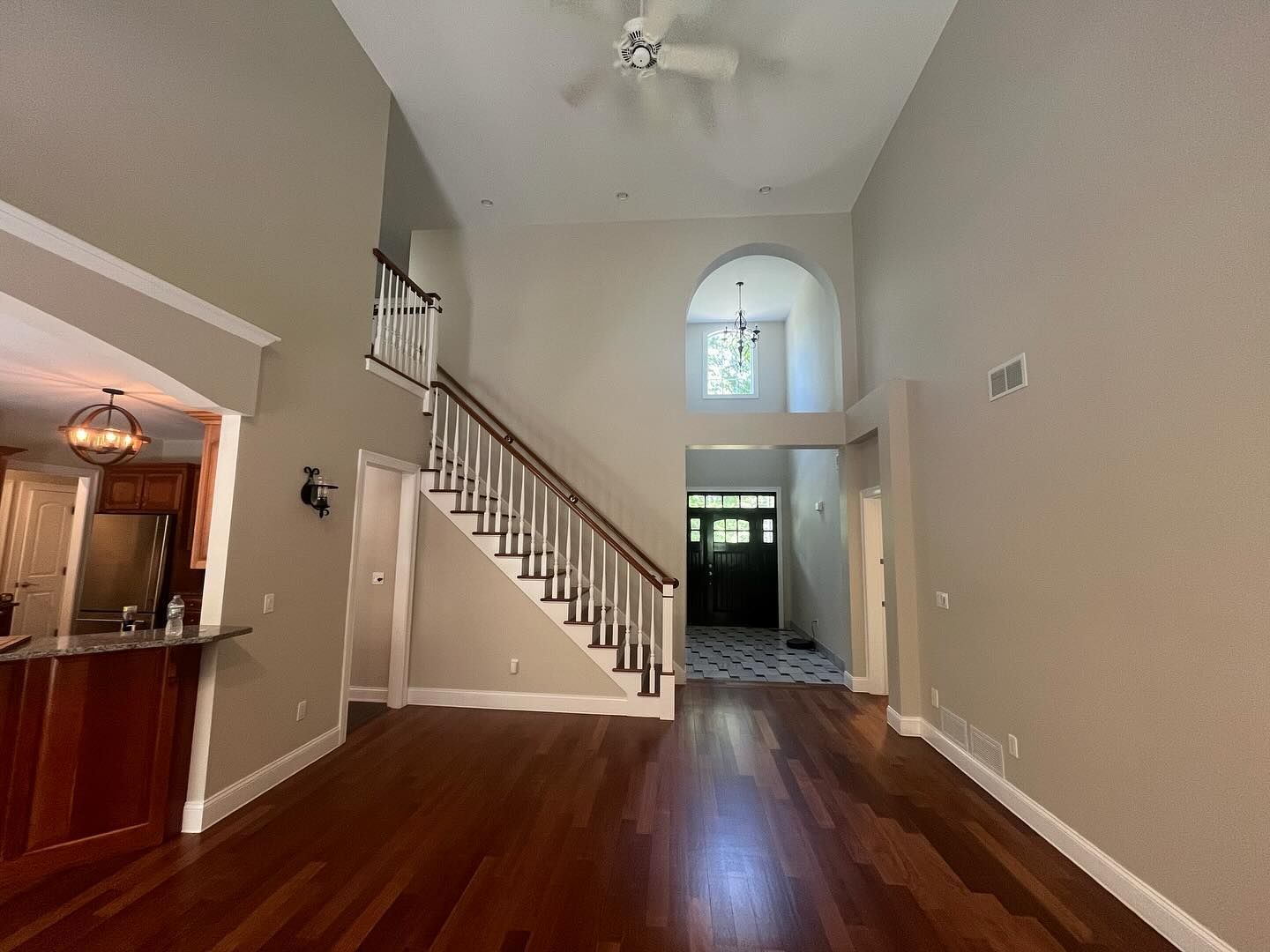 Empty living room with wood floors, staircase, and high ceiling painted beige.