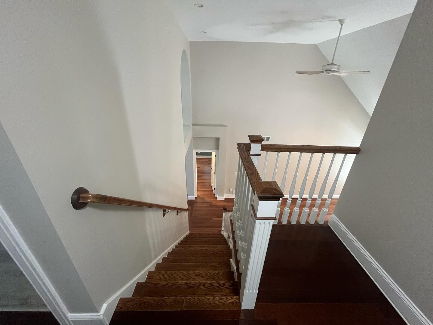 Wooden staircase leads downward. Open space with high ceiling, gray walls, and white railing.