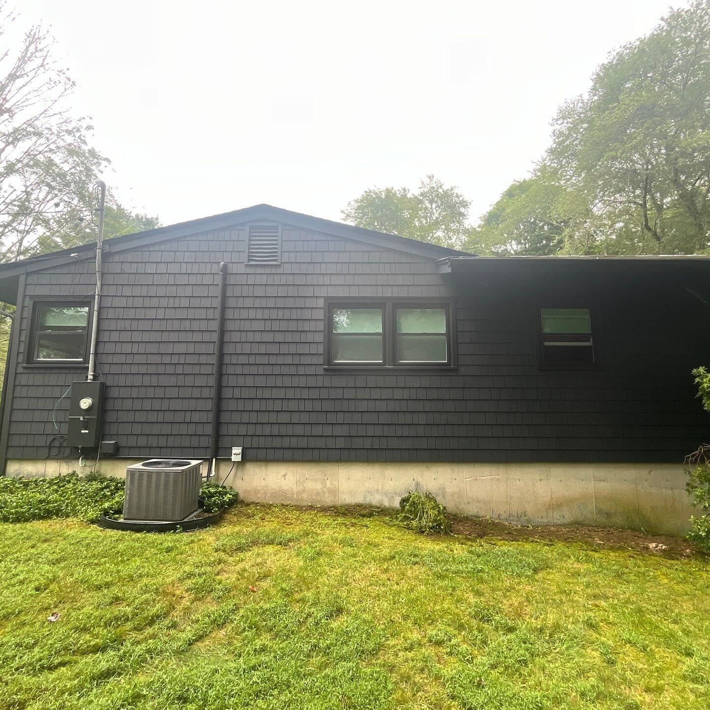 Black-painted house with cedar shake siding, gray foundation, and green lawn.