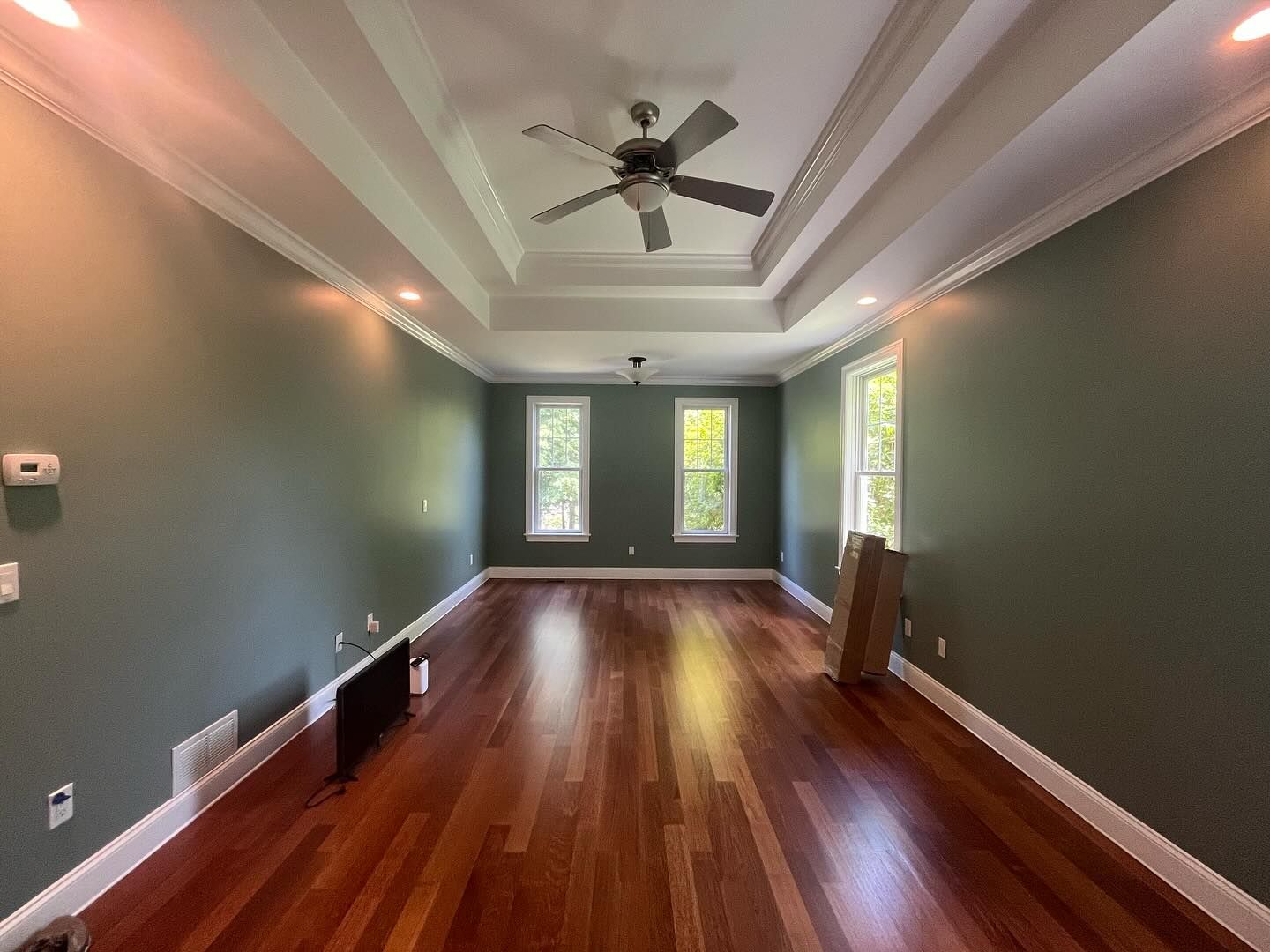Empty room with hardwood floors, green walls, white trim, and a ceiling fan.