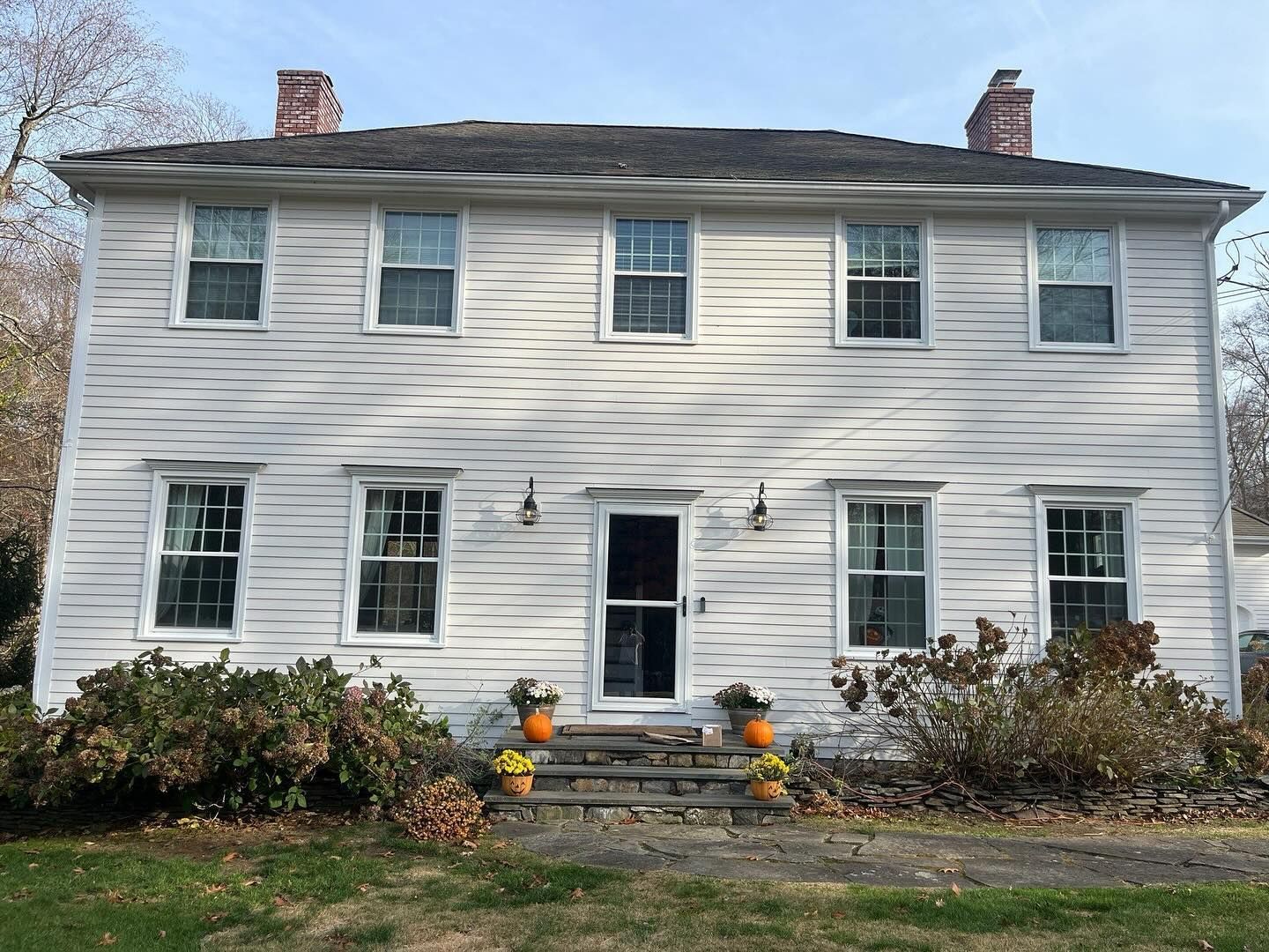 White, two-story house with six windows on each level. Front door centered with steps. Brick chimneys. Sunny day.