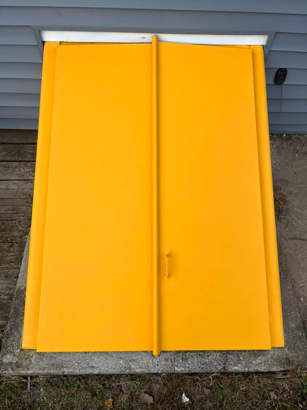 Yellow basement doors against a gray house exterior, set in concrete.