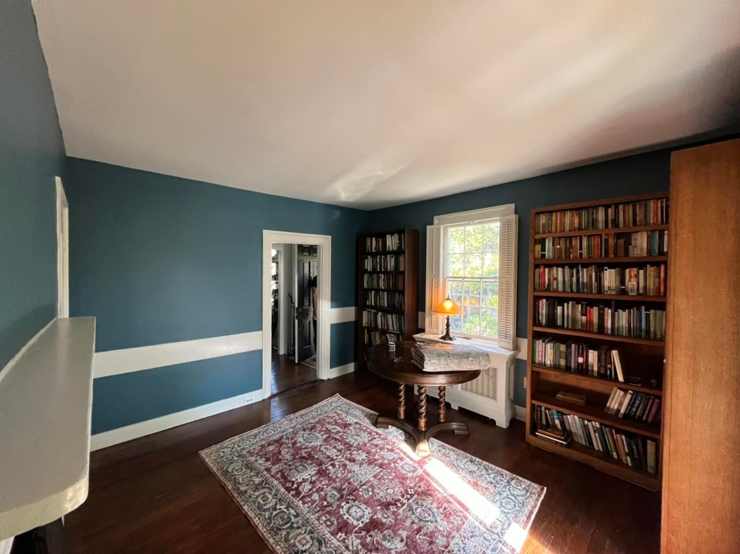 Room with teal walls, bookshelves, rug, and desk by a window.