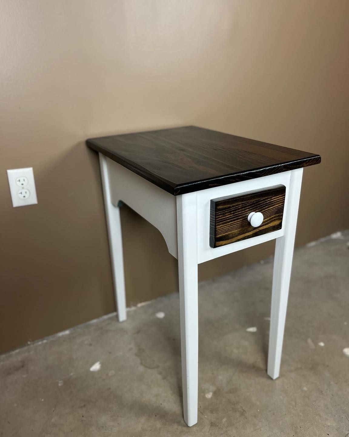 White and black side table with a drawer, against a beige wall.