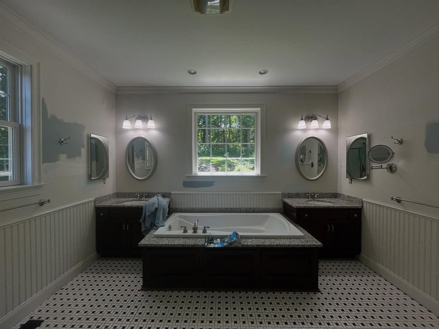 Bathroom with a centered tub, two dark vanities, oval mirrors, and a checkered floor.