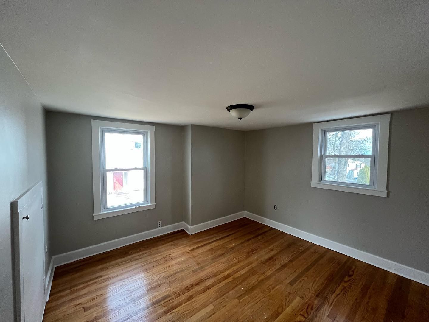 Empty bedroom with hardwood floors, two windows, and neutral-colored walls.