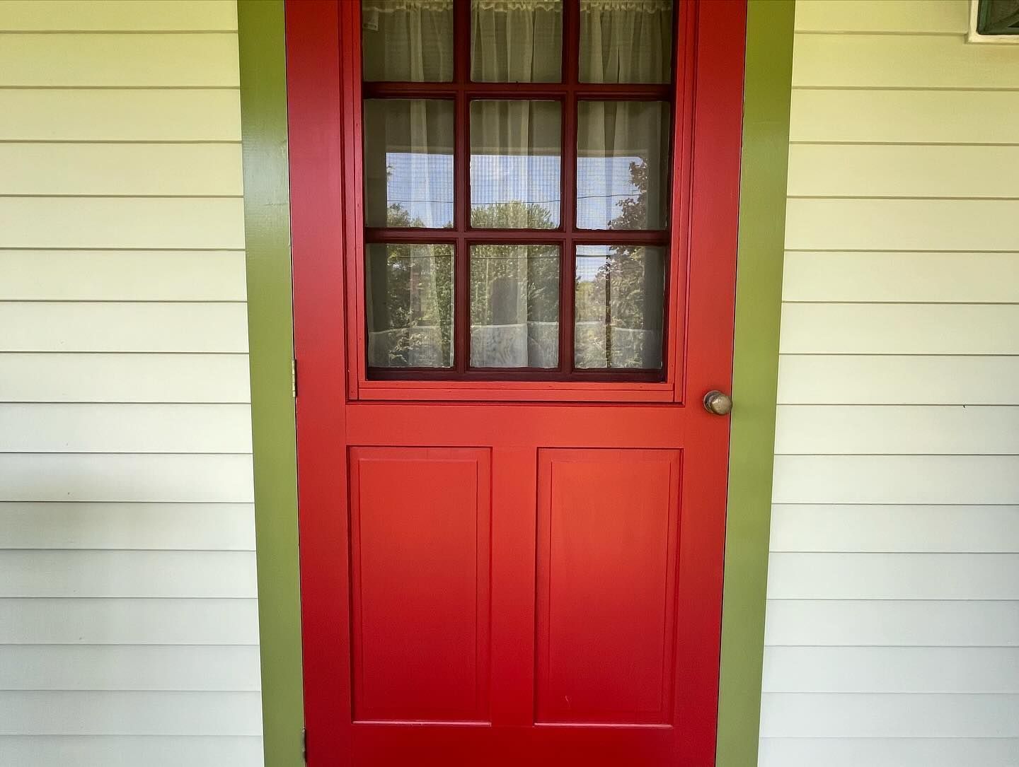 Red door with window, set in a light yellow wall with green trim.