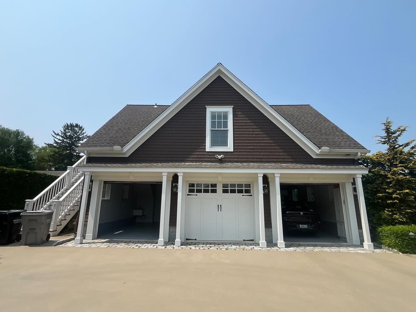 Two-story detached garage with white columns and doors, brown siding, and staircase, under a blue sky.