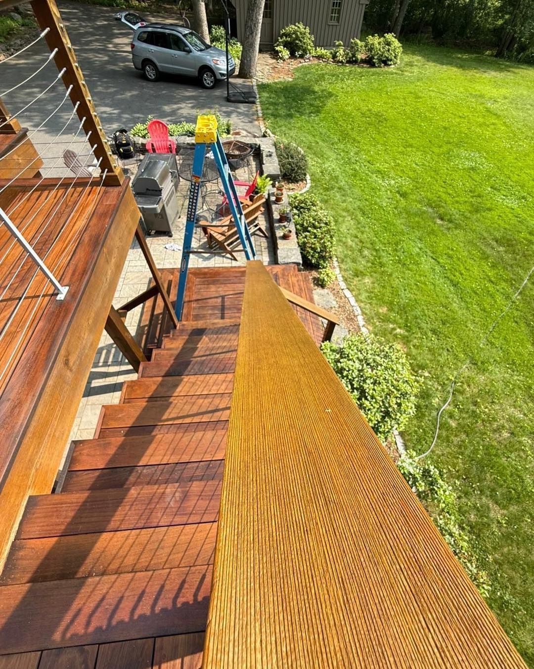 Wooden staircase with handrail leading down to a lawn, driveway and trees in the background.