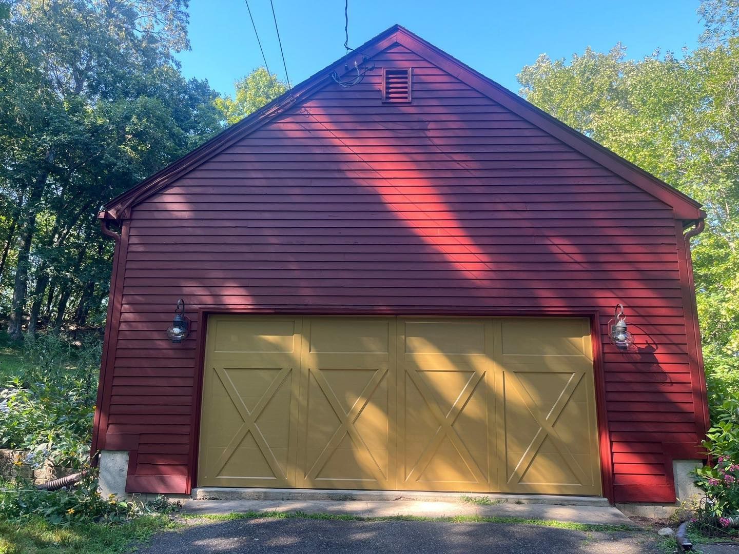 Red wooden garage with yellow door, surrounded by trees under a blue sky.