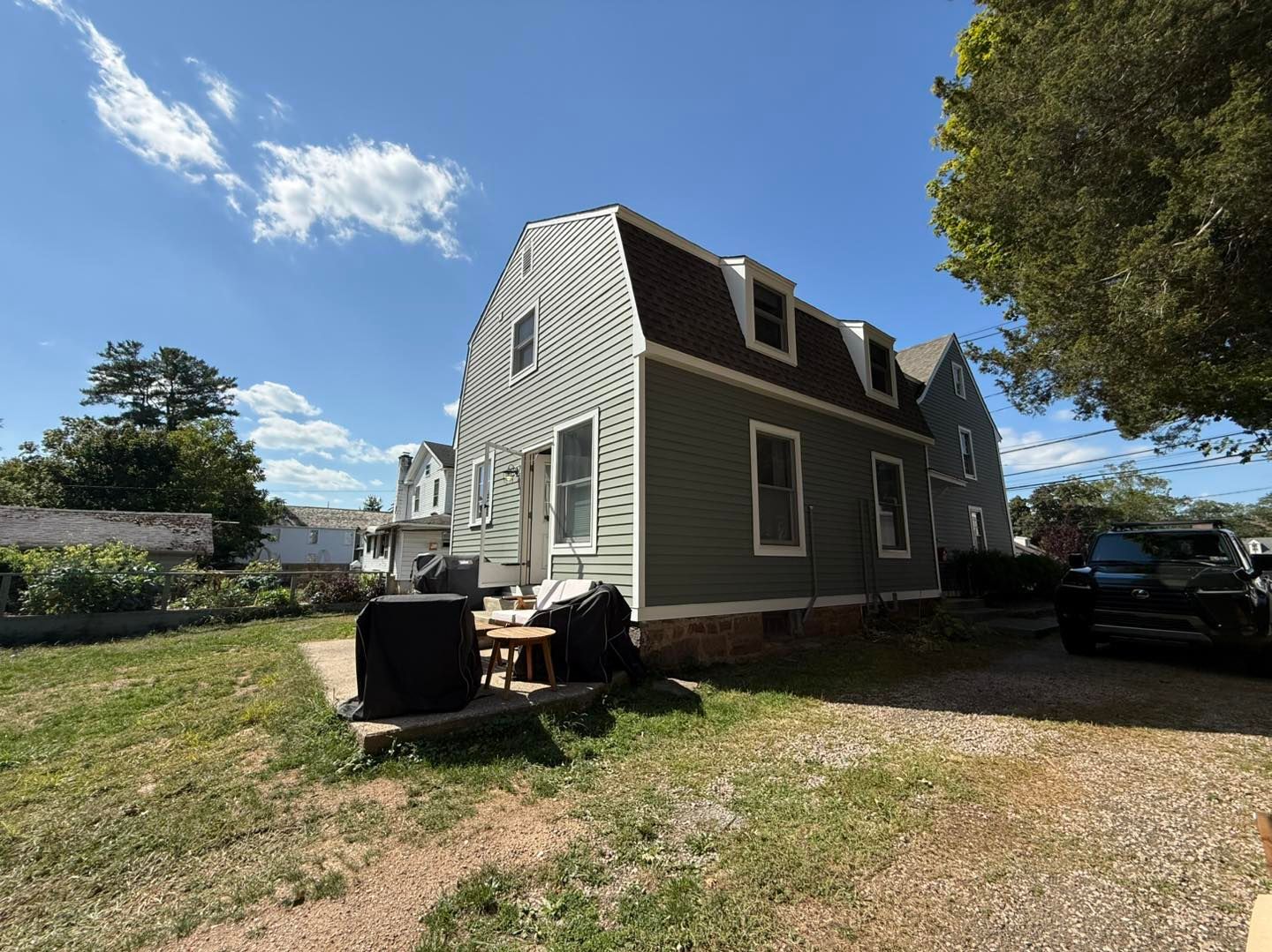 Green house with dormers, brown roof, and small yard on a sunny day.