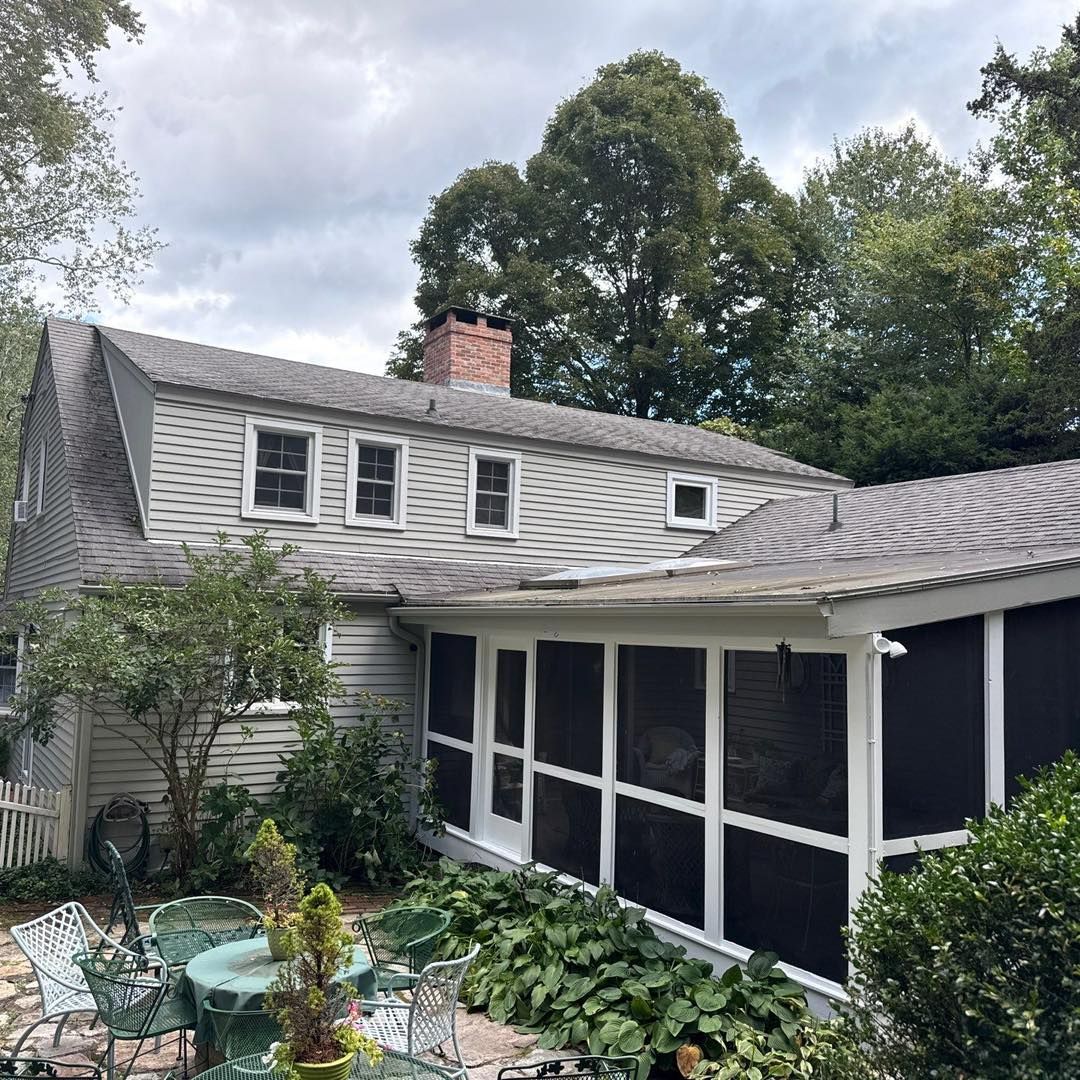 A gray house with a screened porch, surrounded by trees and a patio set. Overcast sky.