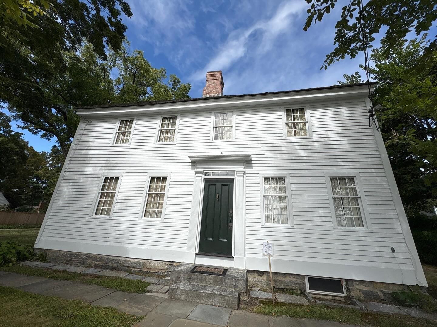 White clapboard house with green door and six windows under a blue sky.