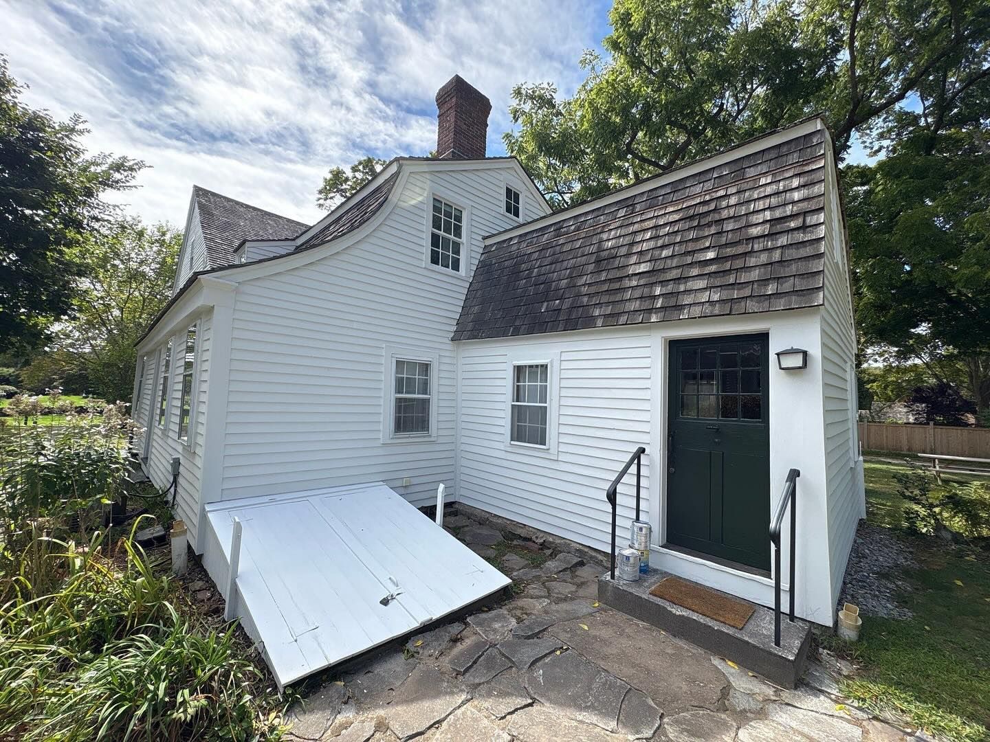 White colonial-style house with green door, wooden roof, and sloped white cellar door, exterior view.