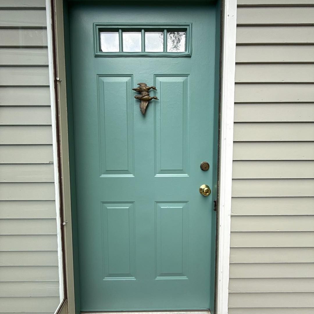 Blue-green door with a decorative knocker and small window, set in a light gray siding.