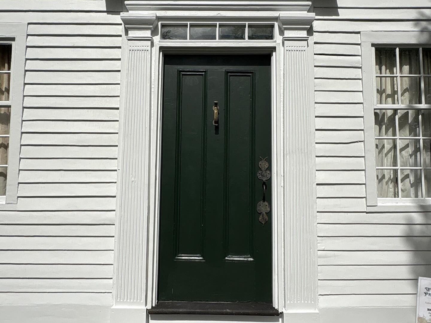 Green door with decorative trim on white clapboard building.