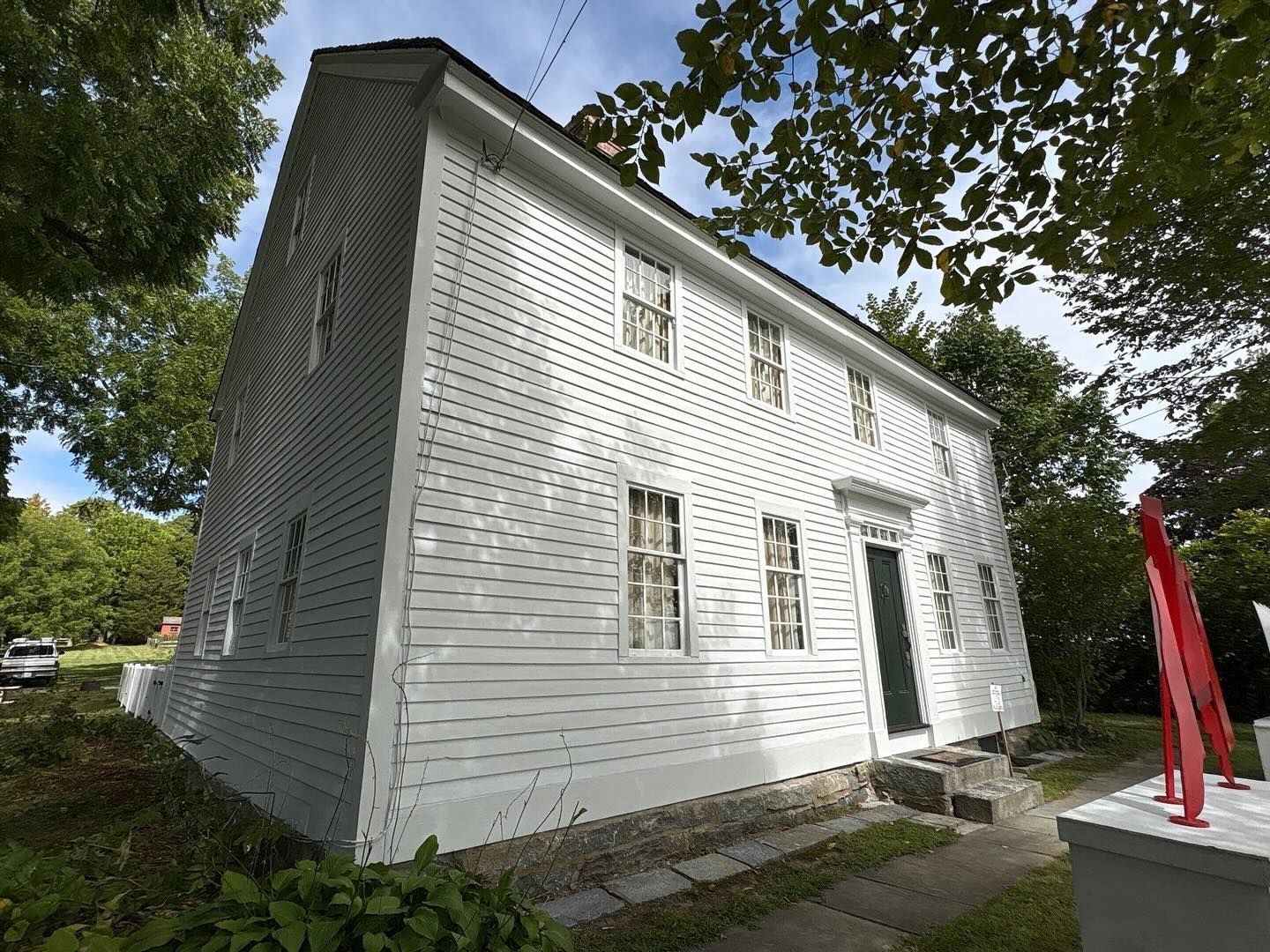 White two-story house with many windows and a dark green door, set under a blue sky.