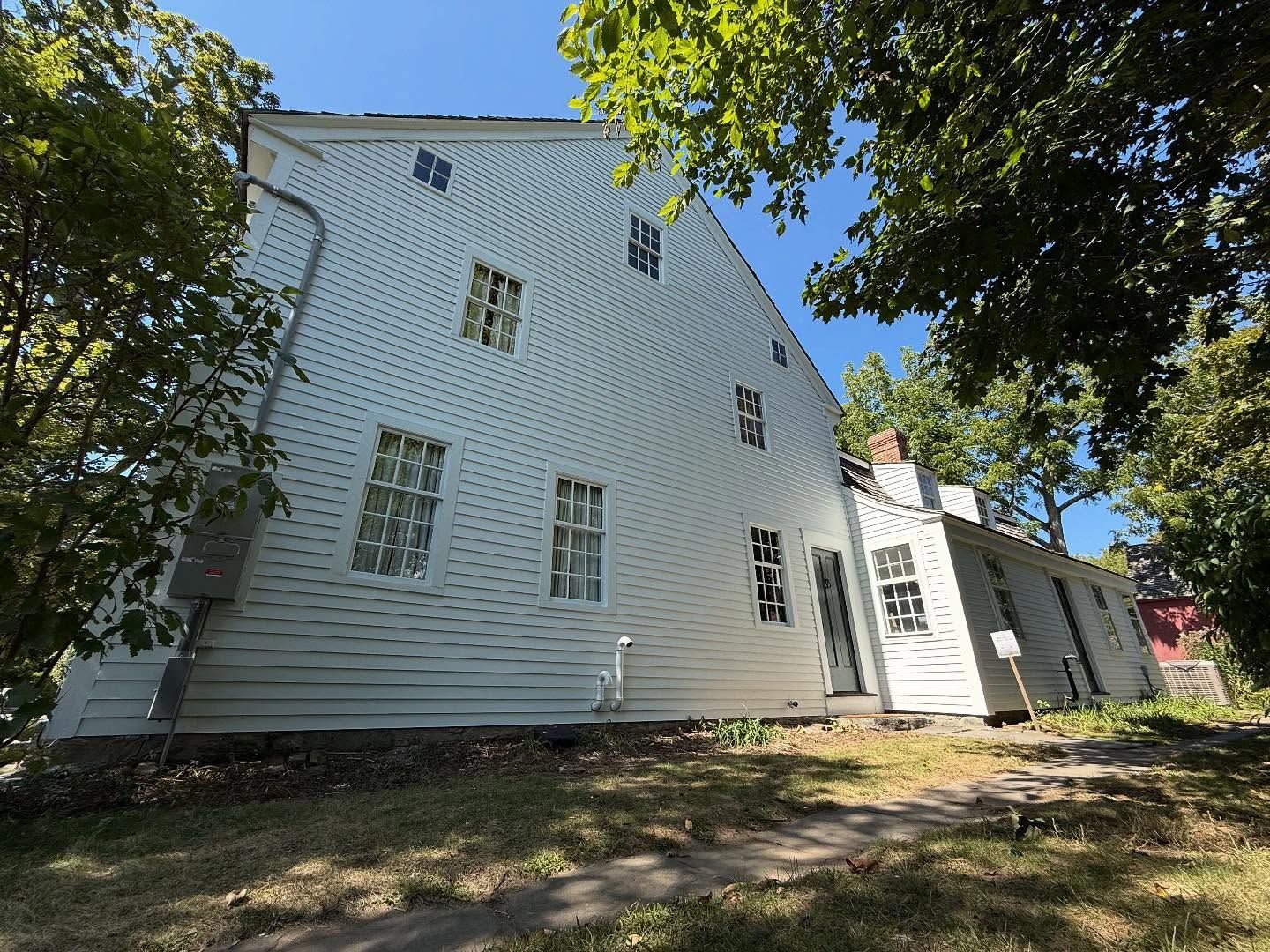 White wooden building with multiple windows, side view, trees, and blue sky.