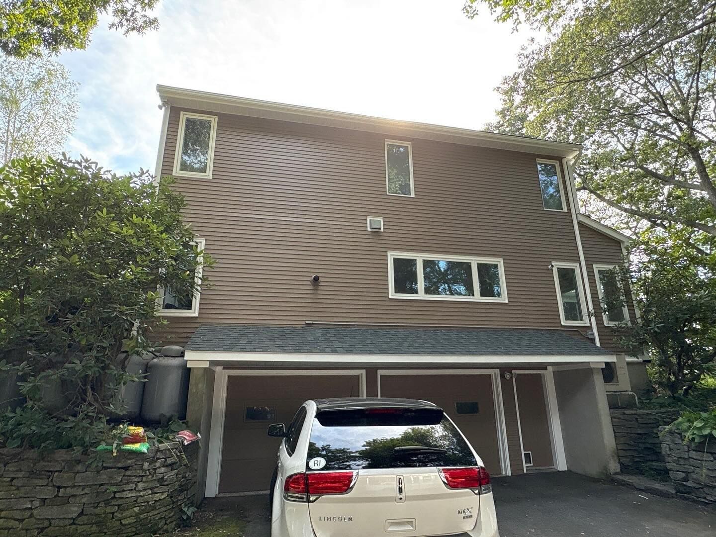 Two-story brown house with white trim.  Car parked in front of two-car garage. Overcast sky.
