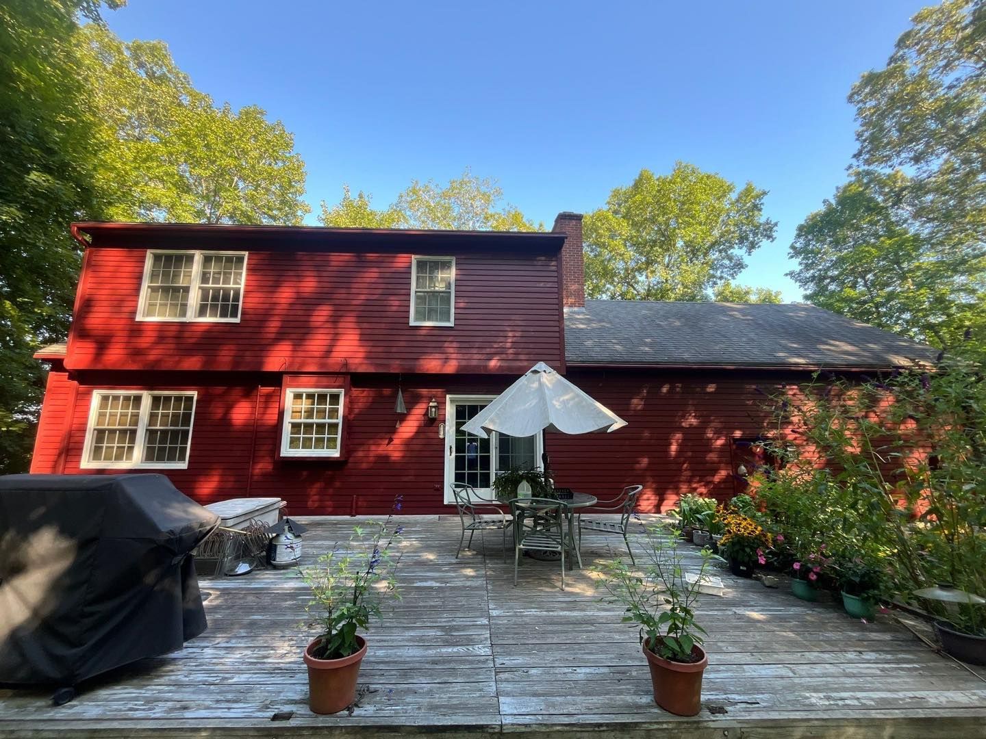 Red house with a deck, patio table with umbrella, and potted plants.