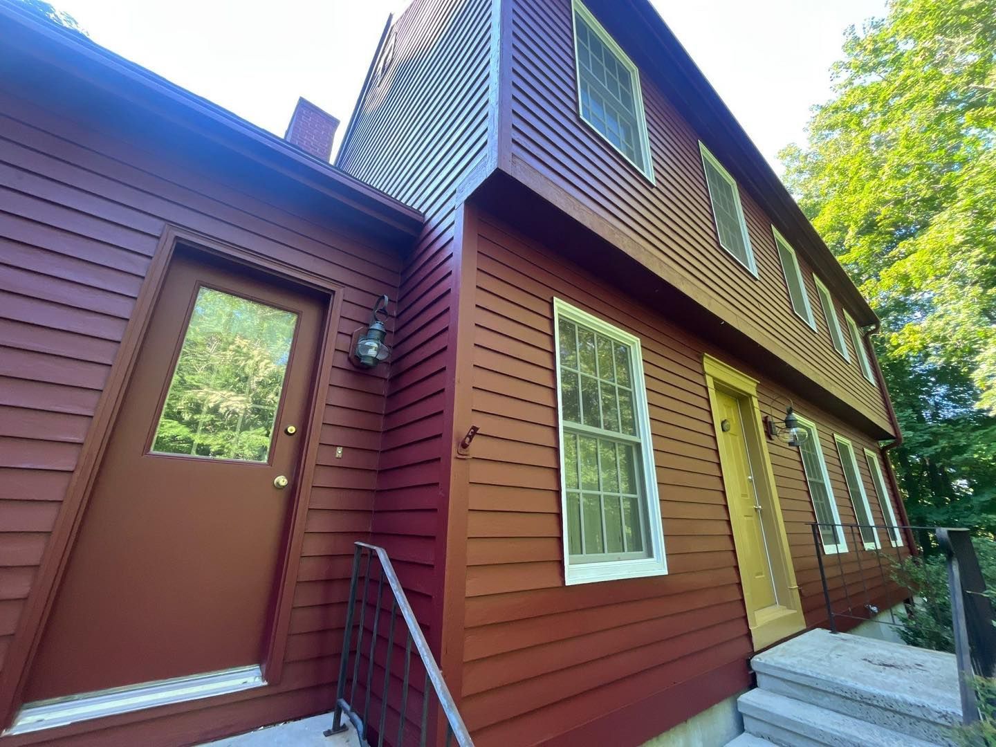 Red clapboard house with two stories, multiple windows, and a brown door.