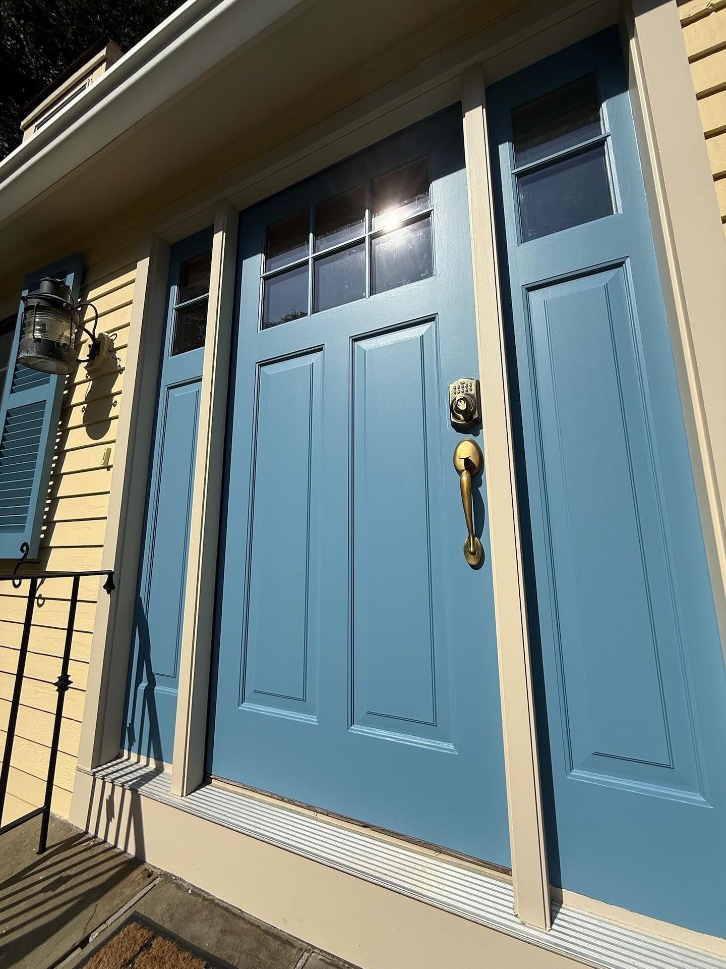 Blue front door with sidelights, brass hardware, and a small transom window.
