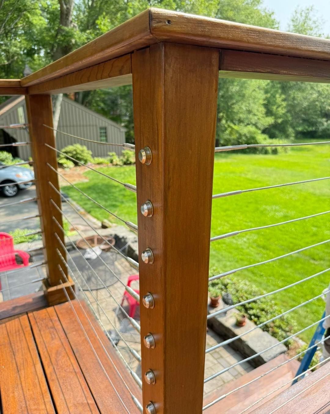 Wooden deck railing with steel cables, bolted to posts, overlooking a green lawn.