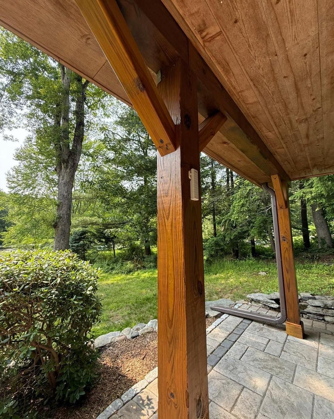 Wooden porch with a view of trees and a brick patio.
