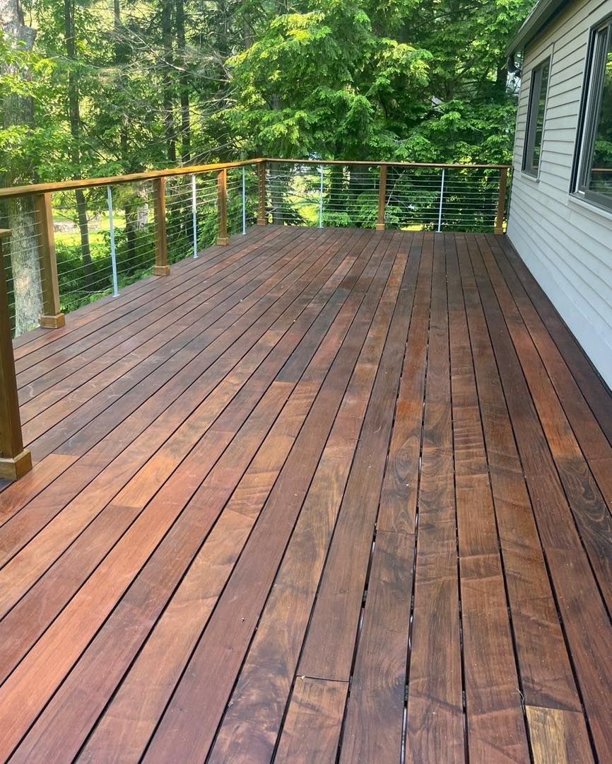 Wooden deck with cable railings; surrounded by trees, connected to a house.