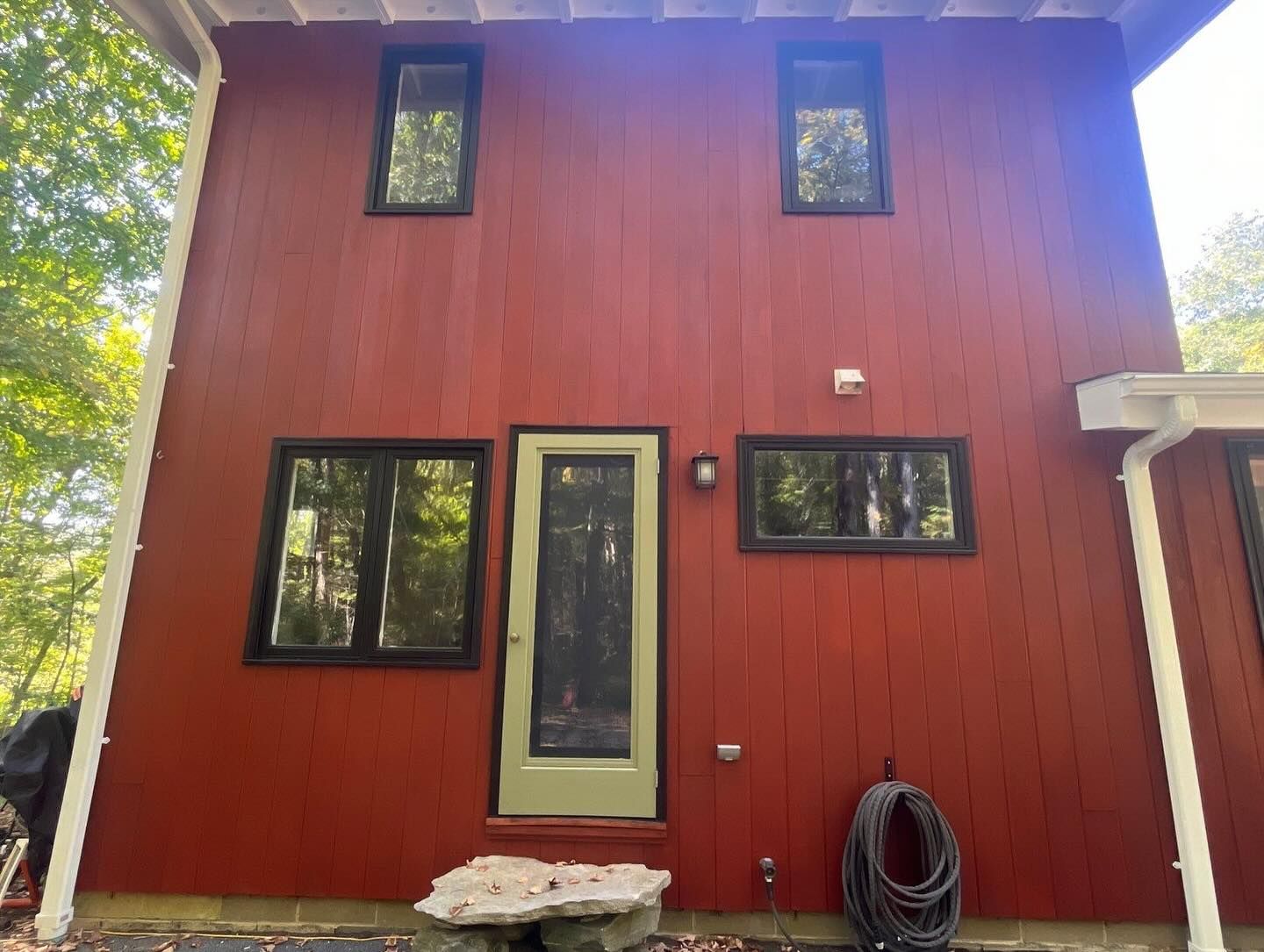 Red-painted house exterior with black-framed windows, a green door, and coiled black hose.