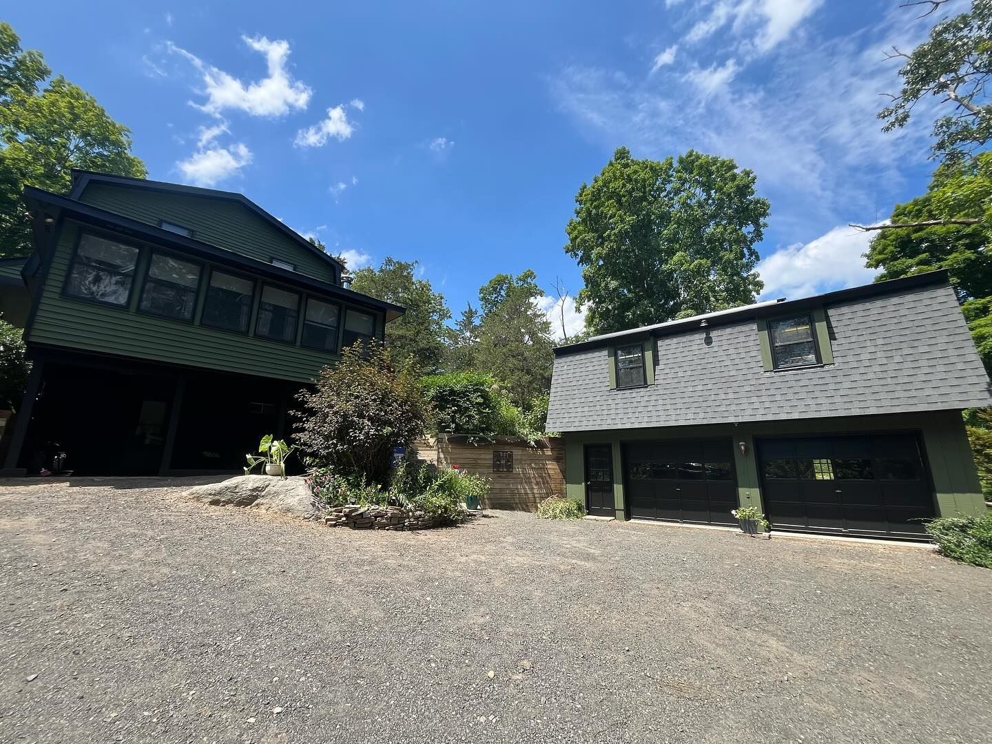 Green house and garage with a gravel driveway under a blue sky.