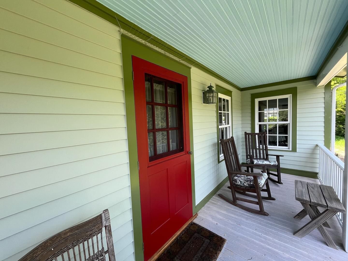 Red door on a green porch with rocking chairs and a wood ceiling.