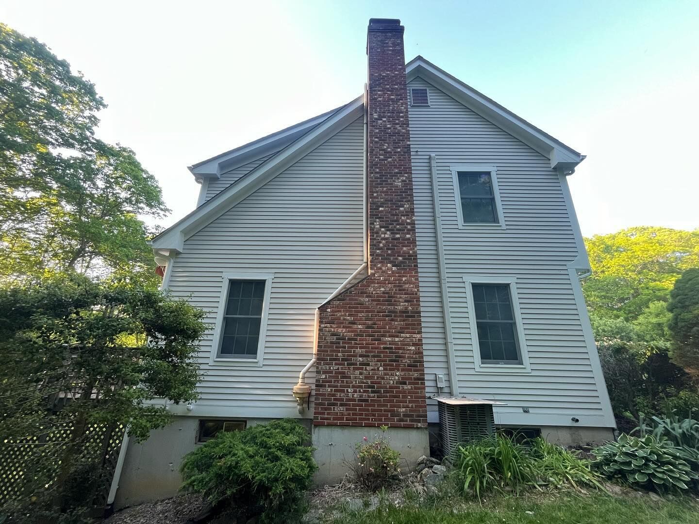 White house with a brick chimney. Green foliage surrounds the building under a clear sky.