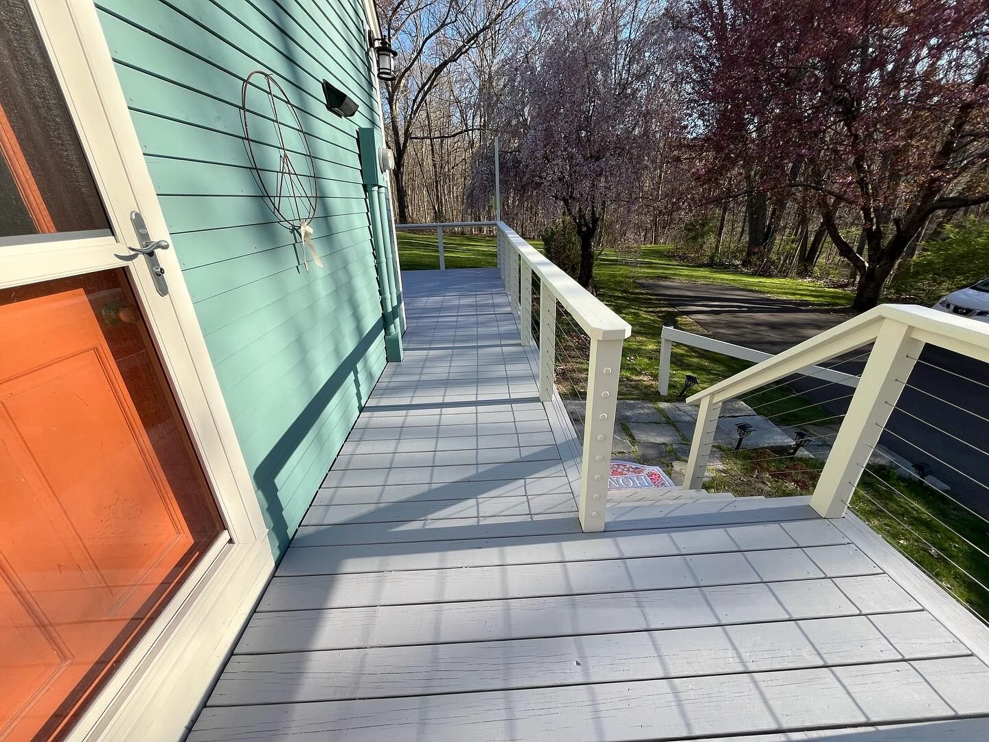 Exterior view of a teal building with a gray deck and white railing. An orange door is visible.