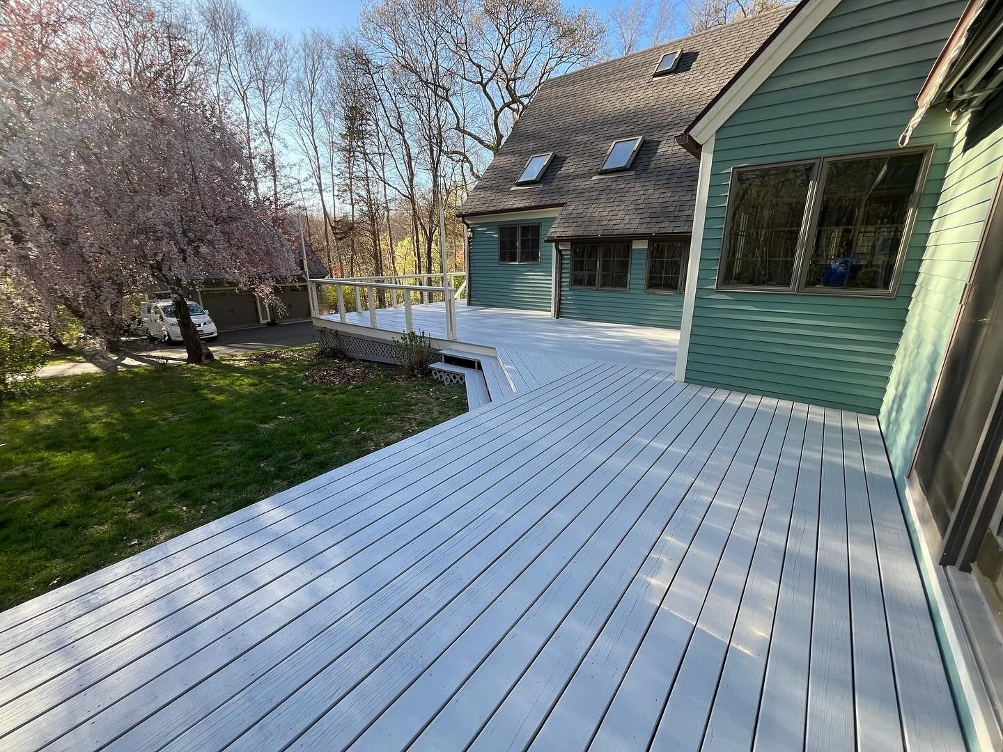 Green house with a large white painted wooden deck, pink flowering tree in the background.