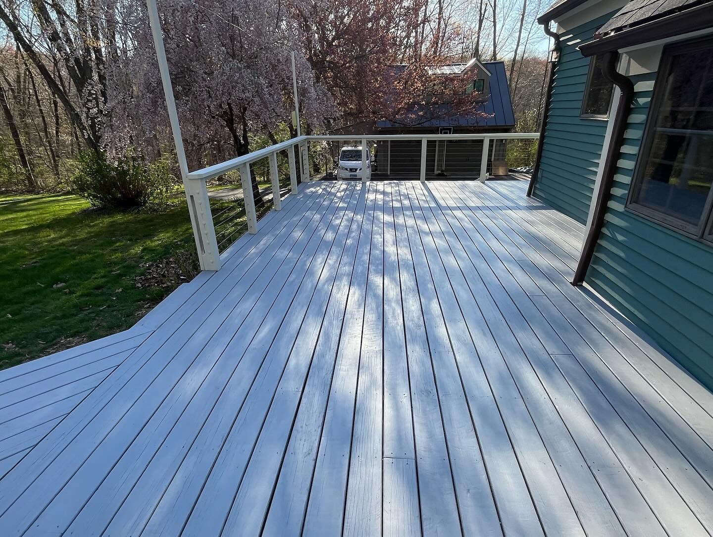 White painted wooden deck with railing, connected to a teal house, sunny outdoor setting.