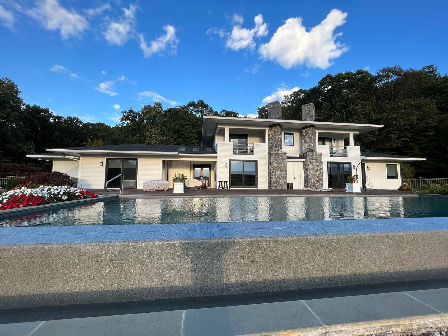 Modern house with a long, rectangular pool in front. Sky and trees in the background.