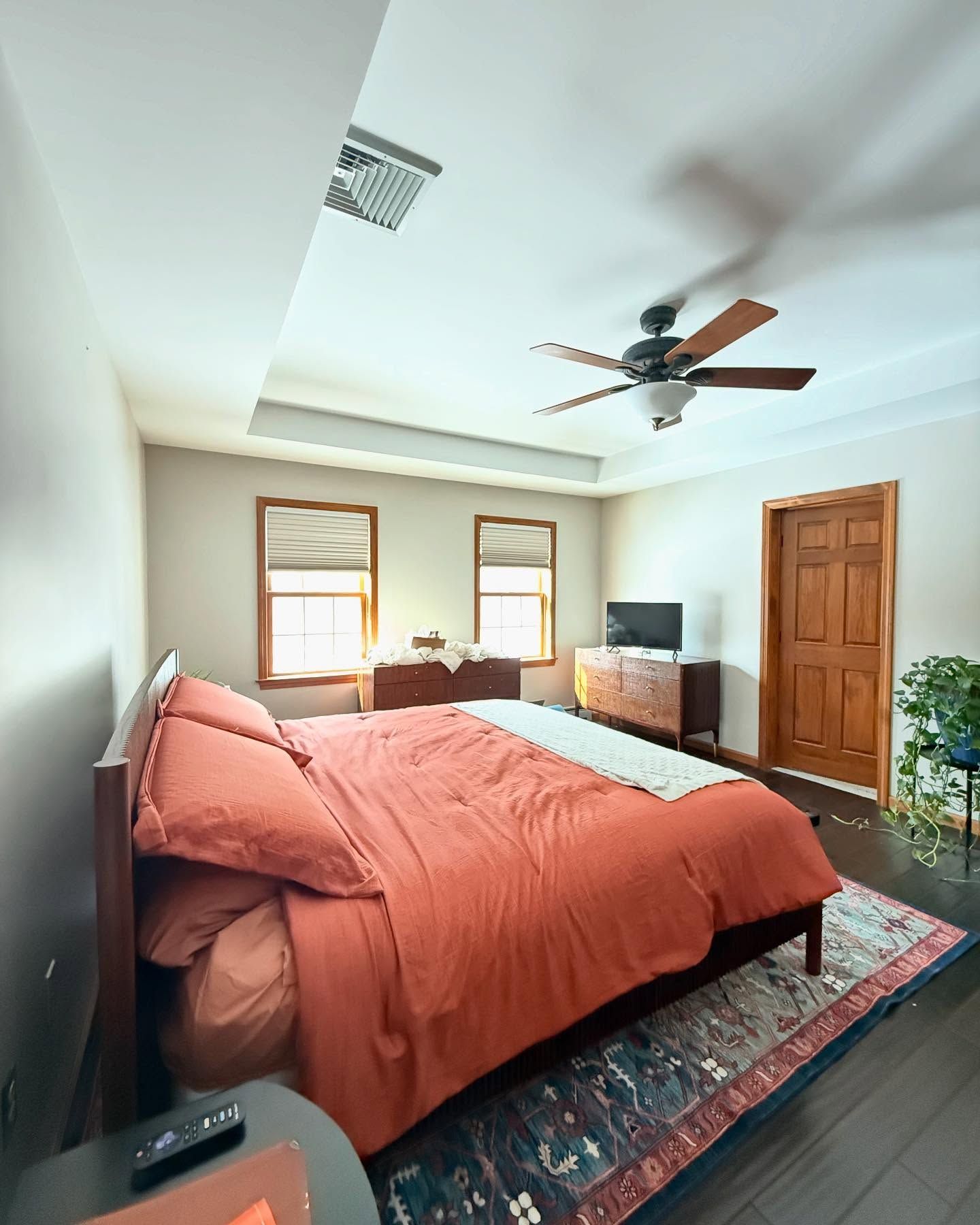 Bedroom with orange bedding, dark wood furniture, and a ceiling fan.
