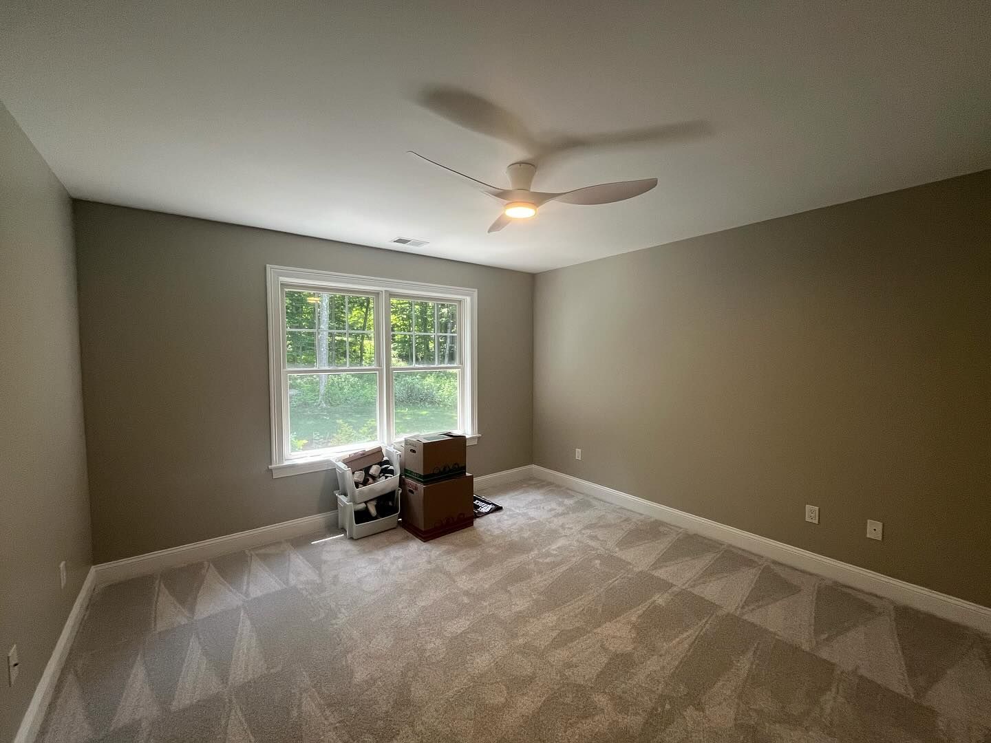 Empty bedroom with beige walls, carpet, and a window. Ceiling fan.