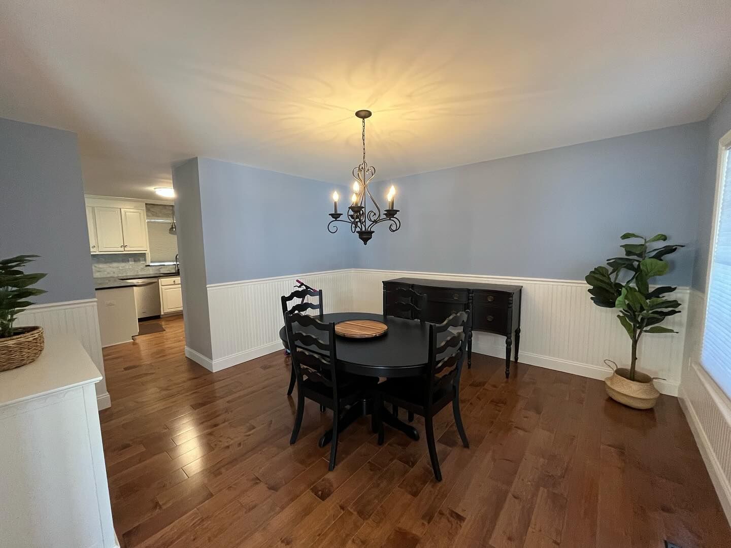 Dining room with wood floor, blue walls, black table and chairs, and a chandelier.