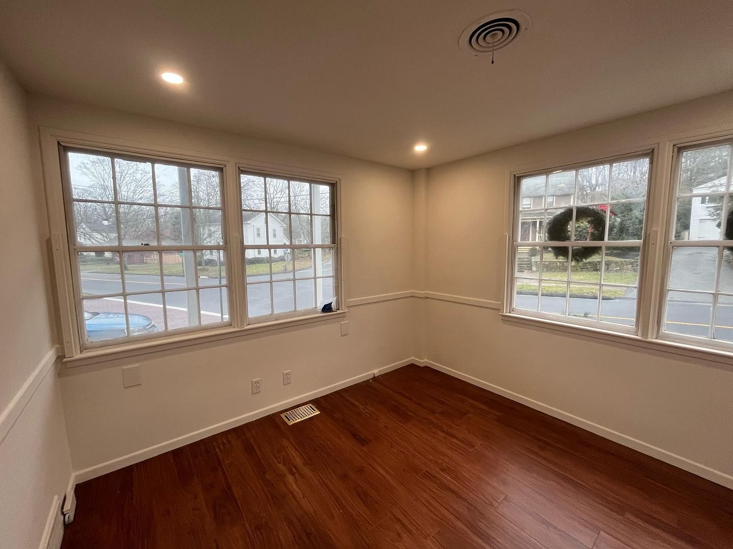 Empty room with wood floors and three windows with white frames.