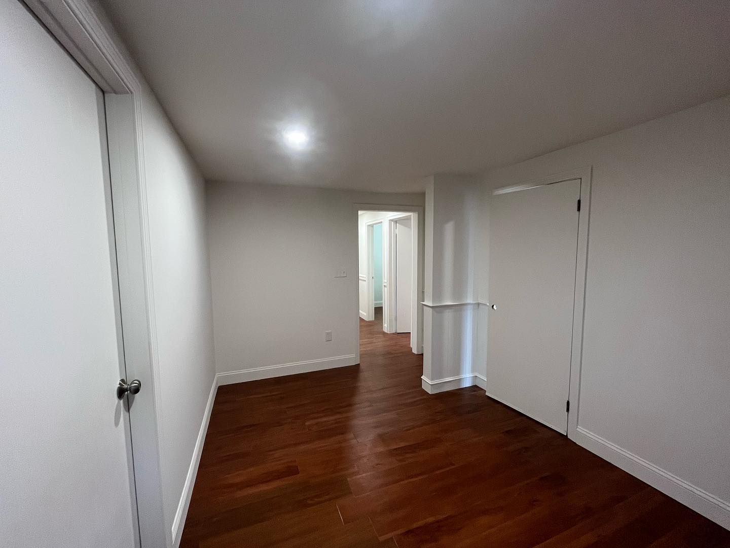 Empty hallway with wood floor, white walls and doors.