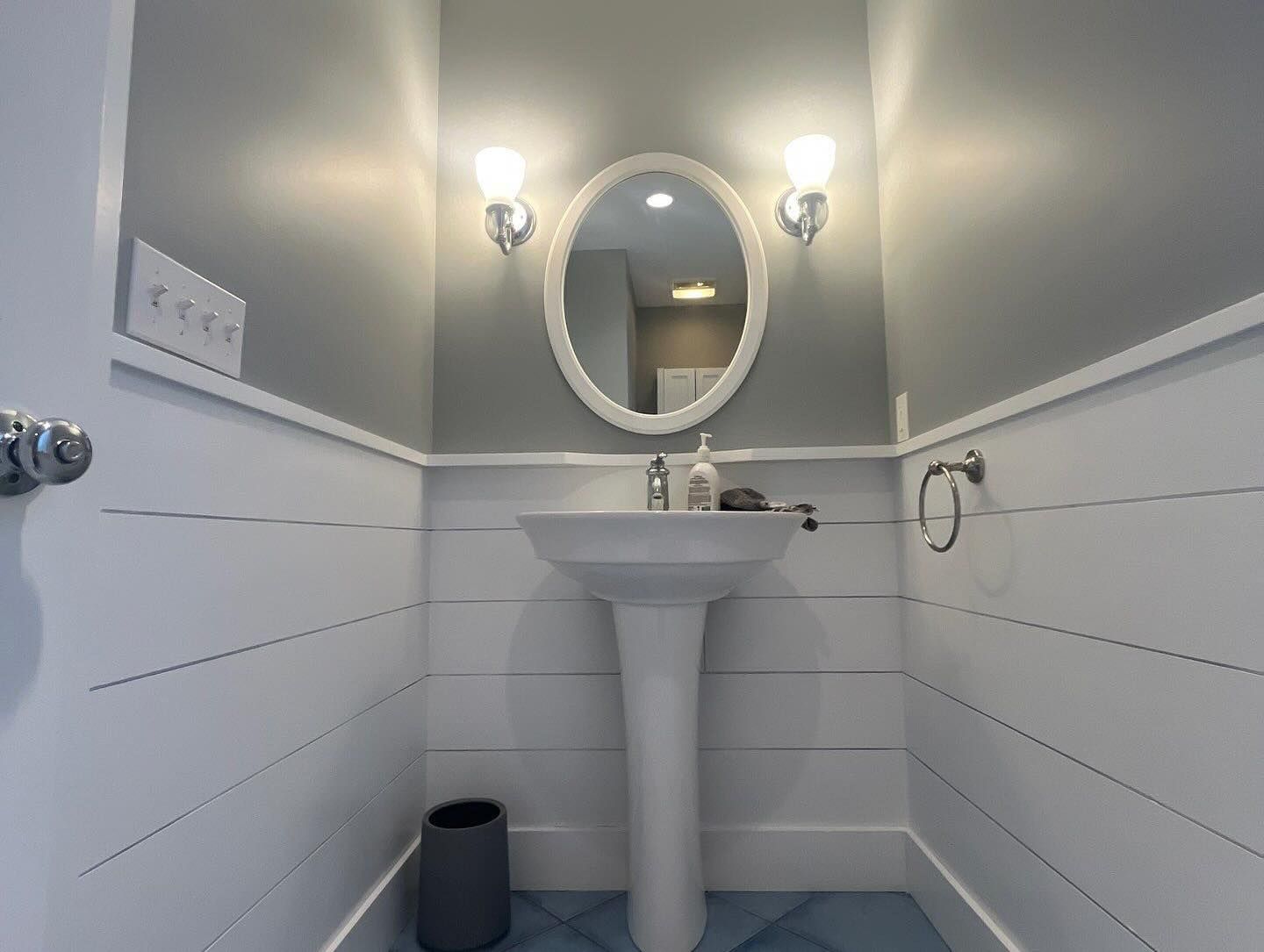 Bathroom with pedestal sink, oval mirror, and shiplap walls, painted blue and white.